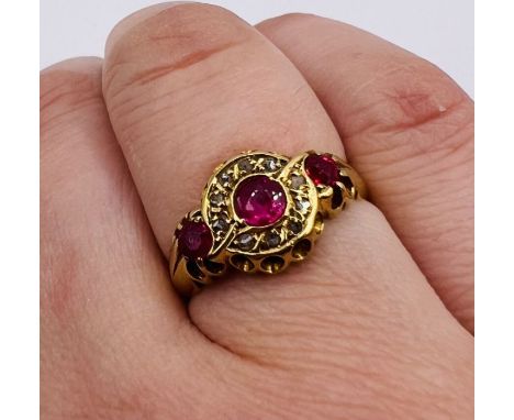 An early 20th century Ruby and diamond set 18ct gold ring. Featuring three rubies, the central stone surrounded by a halo of 