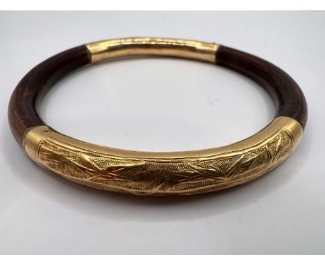 A bamboo and yellow metal bangle. The gold metal is adorned with pictures of bamboo in leaf.