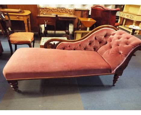 A Victorian mahogany framed arched back chaise lounge having salmon pink button-back upholstery resting on turned supports