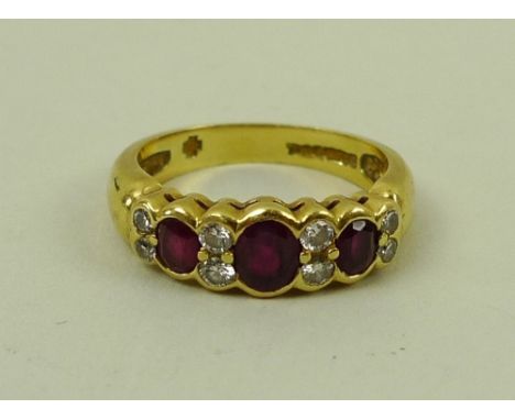 An 18ct gold three stone ruby and diamond dress ring, the central oval ruby flanked by two smaller rubies, divided by four pa