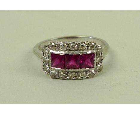 An 18ct white gold, ruby and diamond ring, with three central square cut rubies surrounded in a rectangle by sixteen brillian