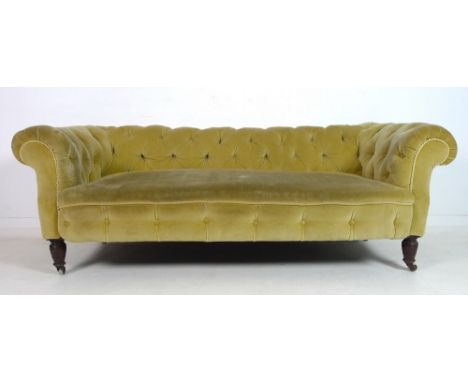 An Edwardian Chesterfield three seater sofa, upholstered in gold coloured buttoned velour with braiding, raised on turned bal