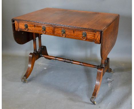 A Regency Style Mahogany Sofa Table, the reeded drop flap top above two frieze drawers with lion mask circular brass handles 