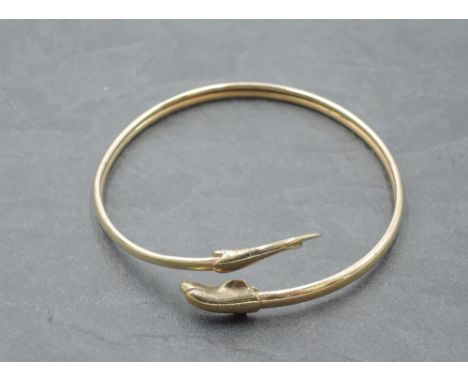 A yellow metal bangle having moulded dolphin knops, no marks tests as 9ct gold,  approx 6.3g