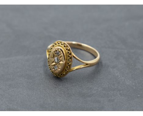A Victorian/Edwardian yellow metal ring stamped 15ct having a trilogy of diamonds in an oval panel with decorative border to 