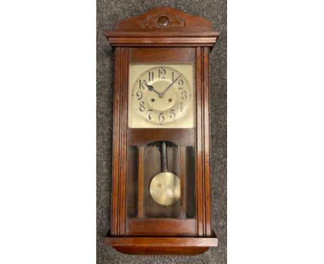 An early 20th century oak cased wall clock, carved cresting, silvered face with Arabic numerals, glazed door, pendulum, 81cm 