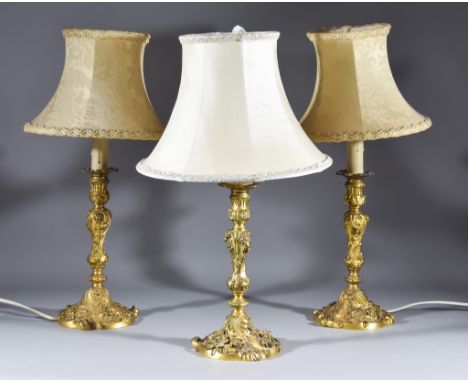 Three French Gilt Brass Candlesticks of Louis XV Design chased and cast with floral leaf scroll and shell ornament, with knop