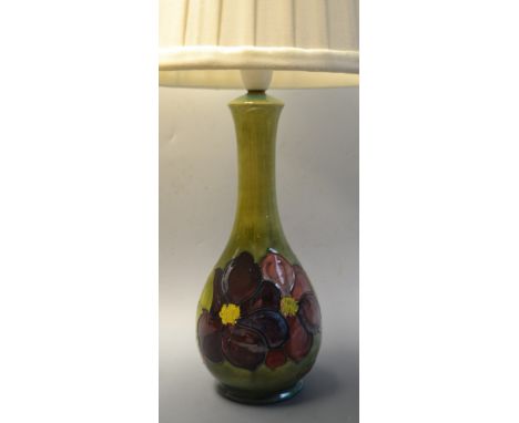 A Moorcroft Clematis pattern table lamp, tube lined with large flowerheads, in tones of purple and red on a mottled green gro