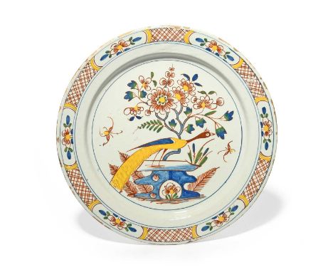 A Bristol delftware charger, c.1740, brightly painted in red, yellow, blue and green with a peacock perched on rockwork besid