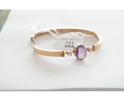 A Russian gold, amethyst and paste set bangle, the oval cut amethyst in claw setting flanked by two claw set colourless paste