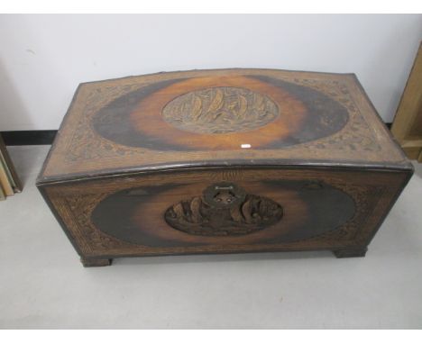 A domed top Oriental camphor wood trunk,  with central carving to top and front panel depicting figures in sailing vessels, 1