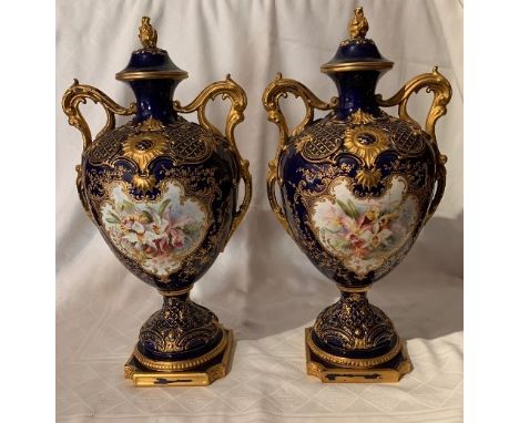 A pair of Royal Worcester covered vases on pedestals, decorated with a rich blue and gilt ground, reserving panels of flowers
