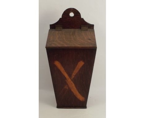 An Antique oak candle box, of tapered rectangular form with sloping hinged lid, the front inlaid with crossed knife and two p