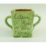 A EWENNY SLIPWARE POTTERY TWIN HANDLED MEAD CUP square based, mottled lime green glaze, with