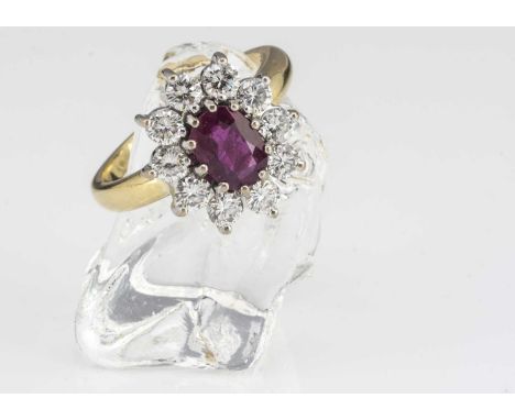 An 18ct gold ruby and diamond cluster ring, the oval mixed cut ruby in claw setting surrounded by a bezel of brilliant cut di