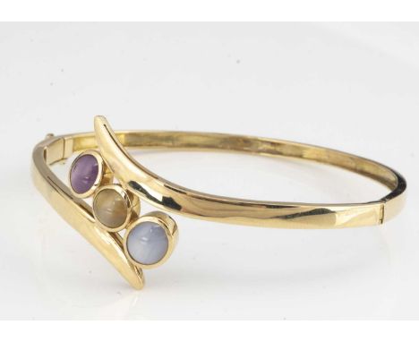 A continental 14k gem set bangle, the crossover cabochons set with a star ruby, star sapphire and centred with a chrysoberyl 