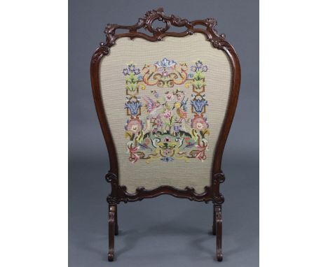 A Victorian carved mahogany firescreen, the pierced foliate scroll frame inset gros-point needlework panel, &amp; on four ree