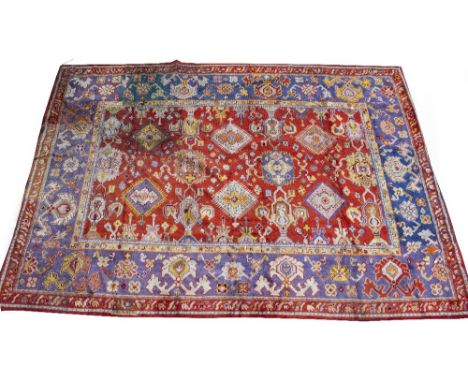 AN ANTIQUE TURKISH RED AND BLUE GROUND WOOLLEN CARPET with a banded border and geometric decoration, 442cm x 313cm Condition: