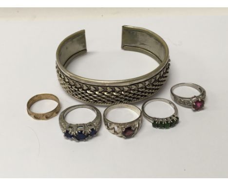 A collection of silver rings set with coloured stones and a metal bangle.