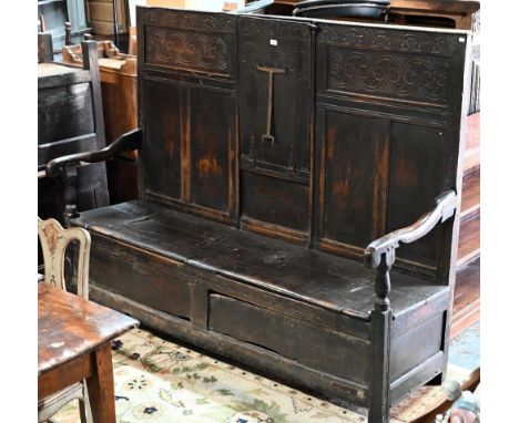 A 17th century oak box settle, the crest rail with lunette carved decoration over further carved panels, unusually centred by