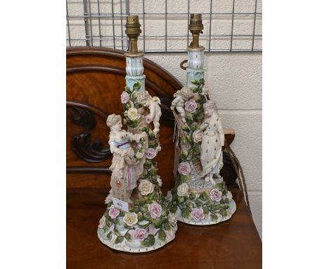 A pair of early 20th century Sitzendorf lamp-bases, modelled with female figures, Cupids and floral encrustaceans, 36 cm high