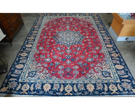 A Persian Mashad carpet with traditional floral design on red ground, navy blue palmette pattern border, 310 cm x 238 cm