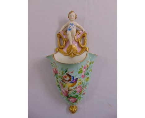A continental ceramic wall pocket decorated with birds and flowers surmounted by a cherub