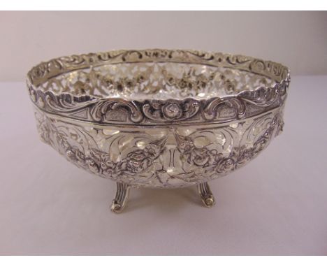 A white metal fruit bowl, circular with scroll pierced sides, chased with floral swags and birds on four pierced bracket feet