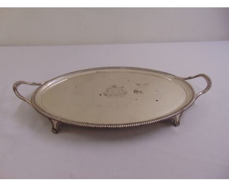 A George III silver oval tea tray, gadrooned border with scroll side handles, engraved armorial to the centre on four bracket