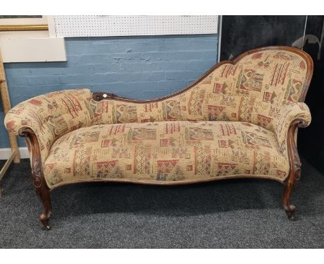 A carved walnut framed chaise longue, having floral and reeded decoration, on scroll feet culminating in castors, tapestry up