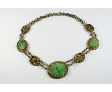 A CHINESE JADE NECKLACE formed with three oval-shaped pierced and foliate carved jade plaques and four oval sections of glass