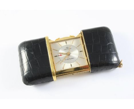 A GILT METAL TRAVELLING CLOCK BY MOVADO the signed square-shaped dial with baton numerals, in a black leather sliding case