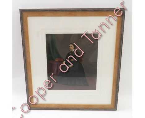 A late 19th Century overpainted photographic portrait of a lady seated at a table and wearing a black dress, 27cms x 23cms