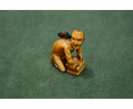 An unusual Japanese carved ivory okimono or netsuke of a crouching man.