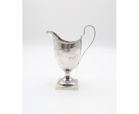 A George III silver cream jug, of helmet form, with cast beaded rim, with engraved scrolling foliate decoration, with a monog