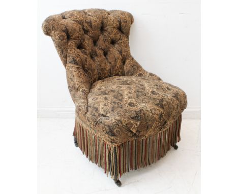 A late 19th century button-back upholstered nursing chair with tassels and ebonised front legs.