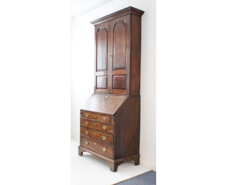 A mid-18th century oak bureau-cabinet: two high fielded panel doors opening to reveal shelves; cleated fall opening to reveal