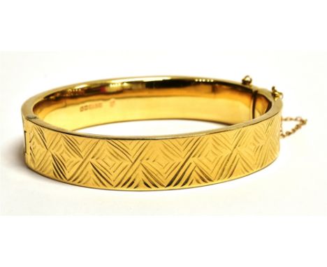 A VINTAGE 9CT GOLD ENGINE PATTERNED BANGLE  The bangle fitted with a safety chin and push clasp, bangle width 1.3cm, hallmark
