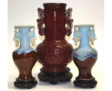 Three Chinese pottery / porcelain vases on wooden stands, comprising of a pair of flambe glaze vases with mask ring handles (