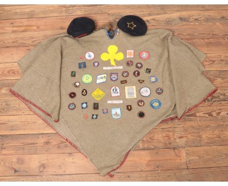 A vintage girl guides poncho, with a large collection of badges and two berets.