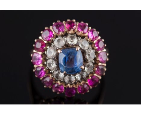 A Ceylon sapphire and ruby mounted circular cluster ring: with central cushion-shaped sapphire approximately 1.25cts, within 