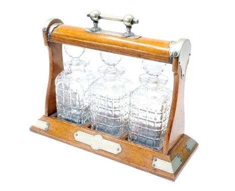An Edwardian oak three bottle Tantalus, with metal mounts, and three associated decanters, 35cm high. 