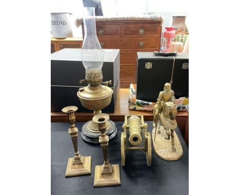 A brass oil lamp on polished black base, a brass model of a cannon, pair of brass candlesticks and a brass knight on horsebac