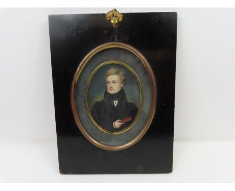 An early 19th century oval miniature portrait on ivory, half length, of a gentleman holding a book, in black frame with acorn