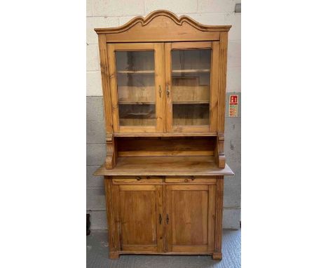 An early 20th century stripped pine dresser having glazed top enclosing shelves, the base with pair of doors enclosing shelf,