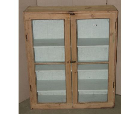 A rustic 19th century stripped pine side cabinet enclosed by a pair of glazed panelled doors revealing a painted and shelved 