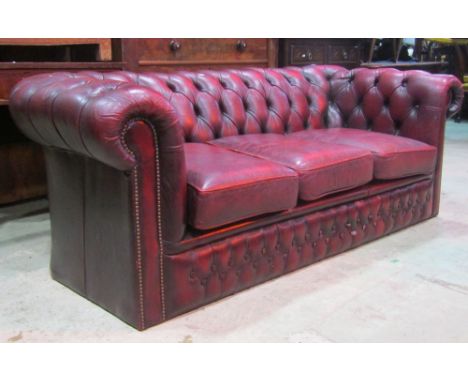 A traditional burgundy leather upholstered Chesterfield three seat sofa, with button back, studded detail and loose seat cush