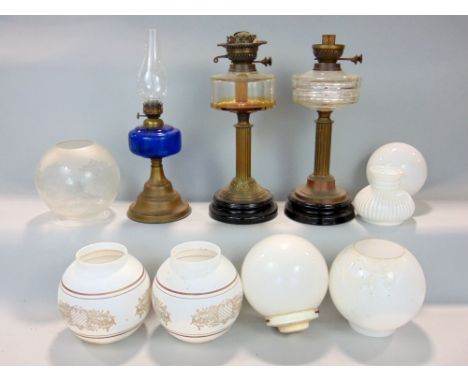 A collection of oil lamps to include two corinthian column lamps and a further lamp with blue glass reservoir and seven shade