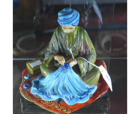 A ceramic figure of a carpet seller, Embroiderer of Kashmir, signed R.  Johnson, H:18.5cm W:17cm D:13cm