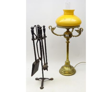 Tall eastern brass converted oil lamp, three winged swan moulded supports, on engraved domed base with amber coloured glass s